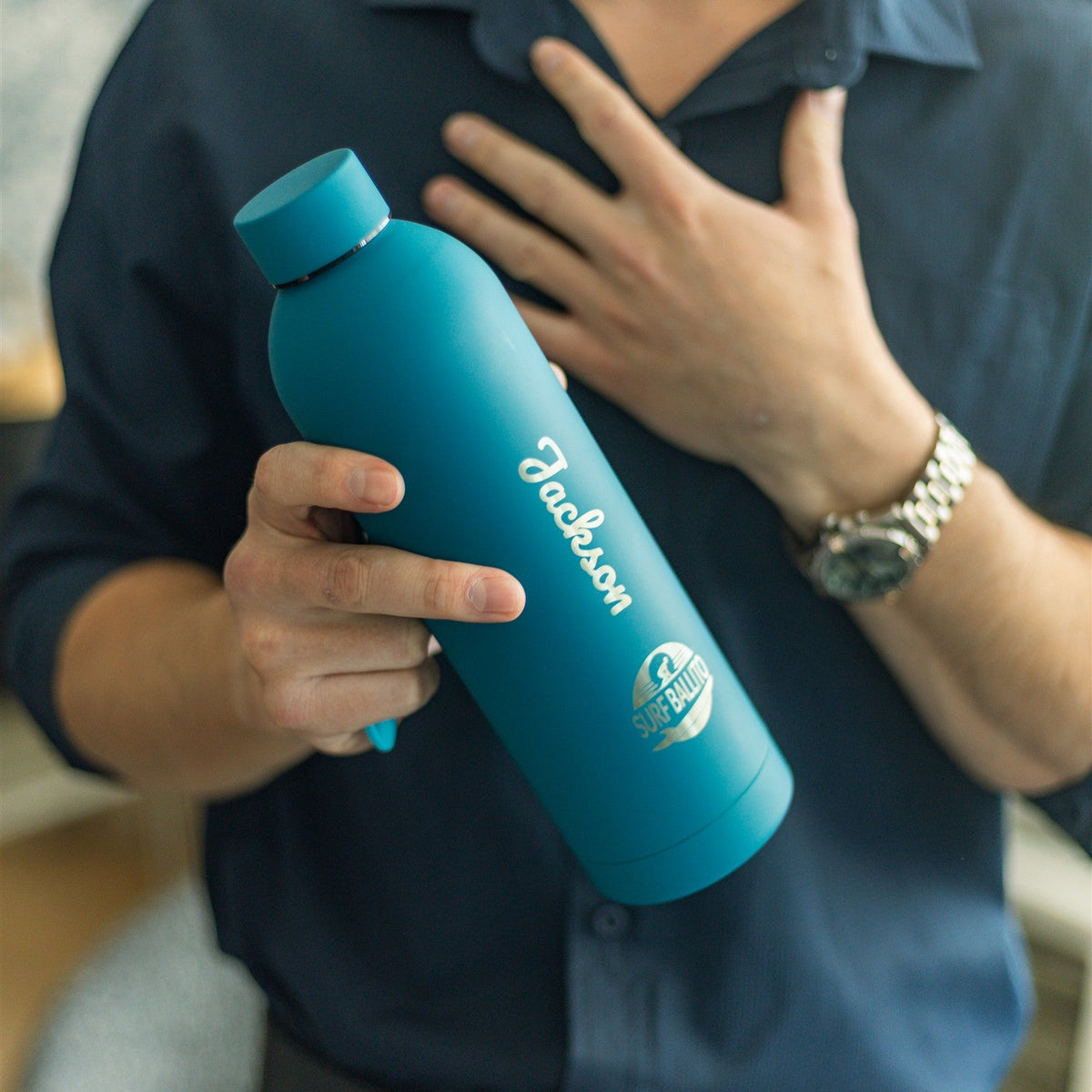 A man holding a turquoise PurePop flask engraved with the name Jackson.