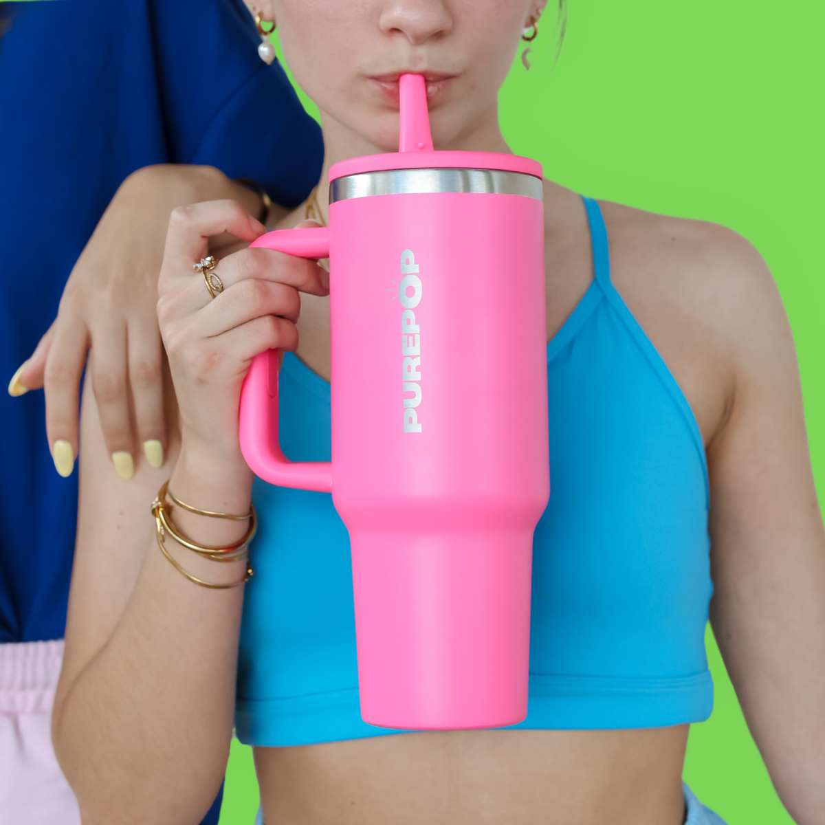 A person wearing light blue athletic shorts and a crop top holds a pink tumbler with a straw and an inflatable pool float shaped like a donut.