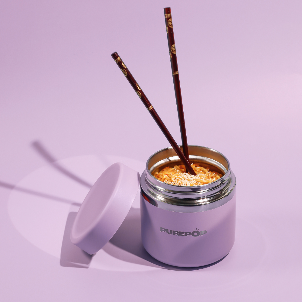 A Purepop Food Flask in Twilight Purple holds noodles topped with sesame seeds and two dark chopsticks, its lid resting nearby on a pastel purple surface.