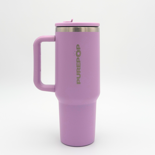 A tall, Soft Lilac Carry Series PurePop™ travel mug with a handle and stainless steel rim stands against a white background. The brand name appears vertically in silver on the side, and the mug includes a secure lid.
