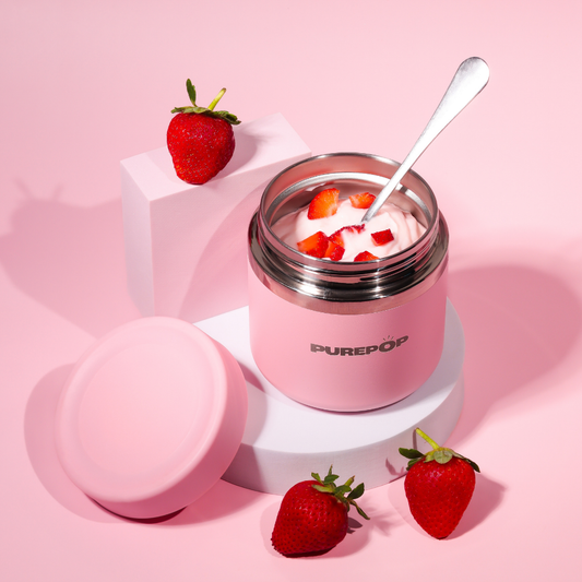 A Purepop Food Flask | Pastel Pink, filled with creamy yogurt and strawberry pieces with a spoon inside, sits among fresh strawberries on pink geometric platforms against a playful pink background.