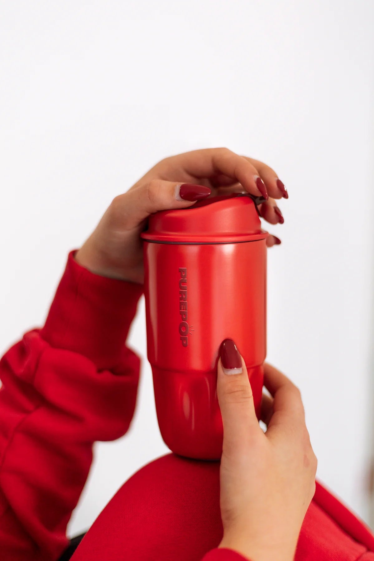 Hands with red nail polish holding a red PurePop Sip Series cup.