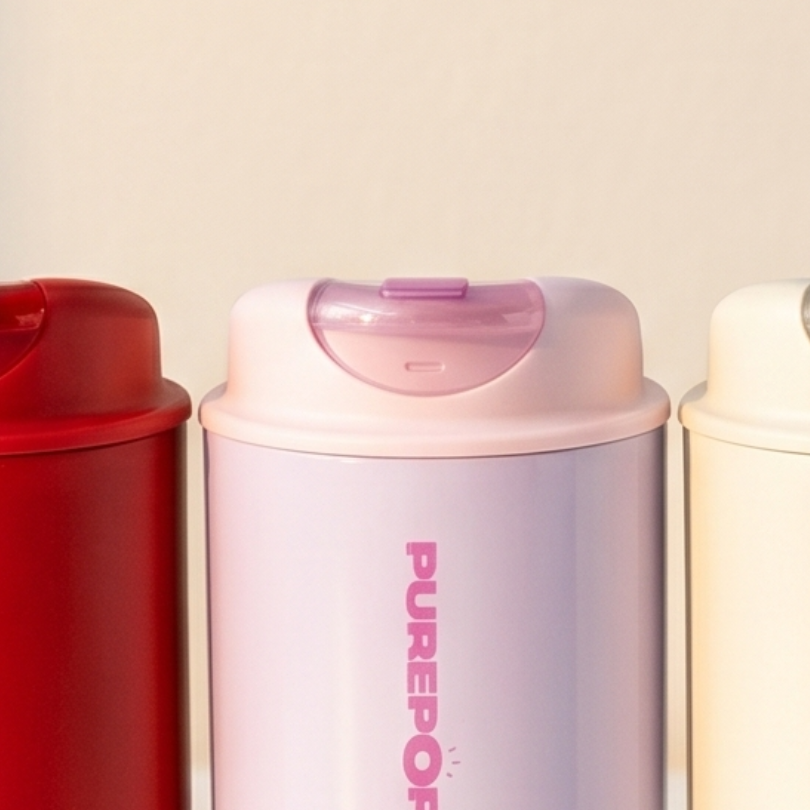 Three cylindrical containers with flip-top lids are shown side by side. The left one is red, the middle one is pale purple with PUREPOP written vertically, and the right one is off-white.